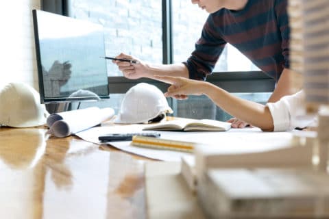 Two engineers working for a construction company reviewing the blueprints at the office.